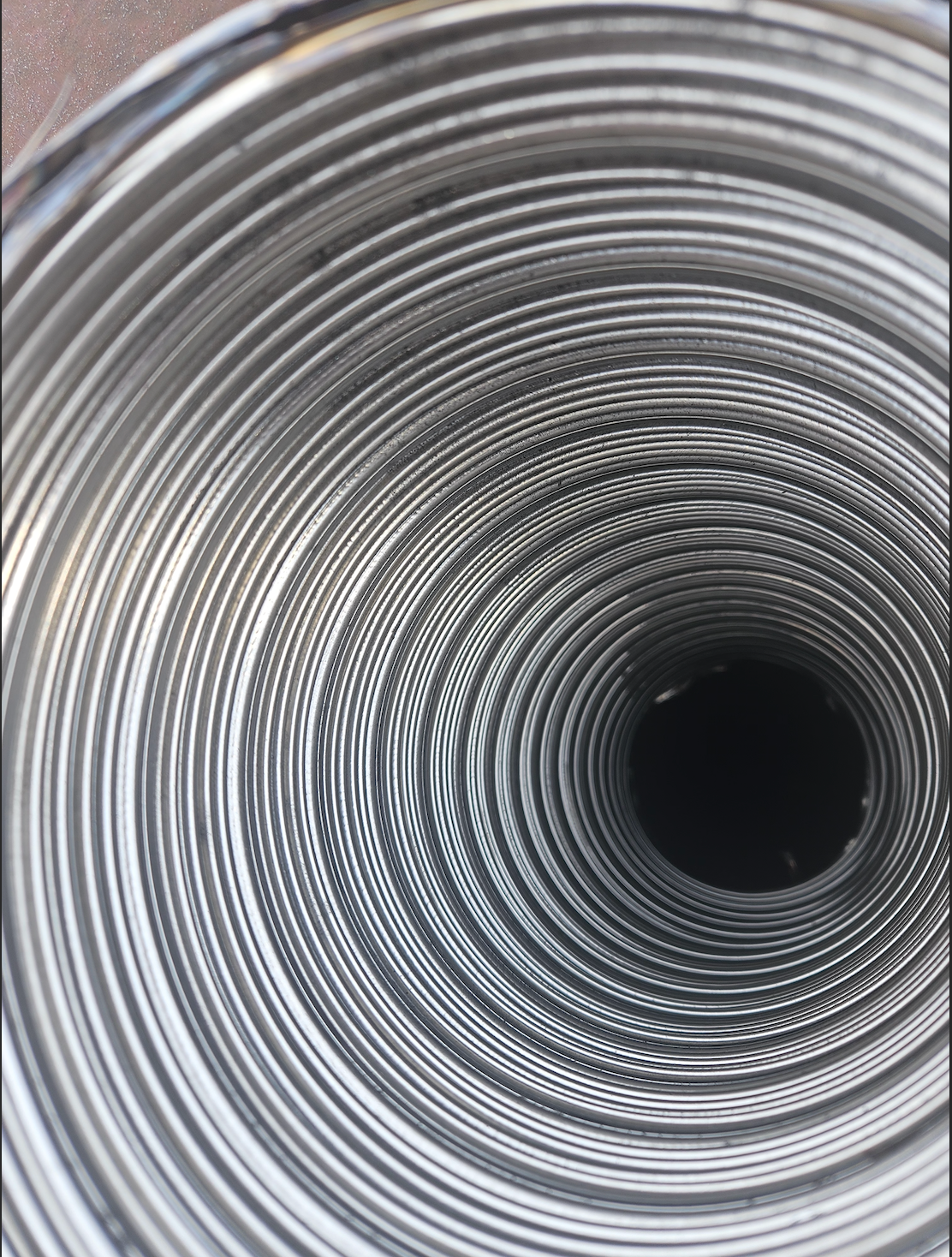 Close-up view down a coiled silver metal pipe with a dark circular opening in the center