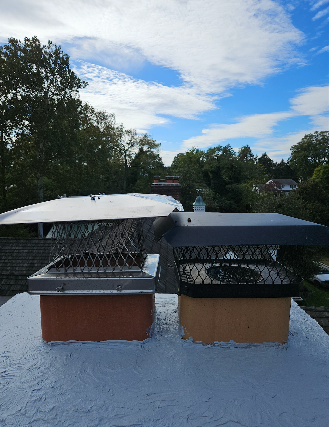 Two rooftop vents with white and dark gray covers on a snowy roof under a partly cloudy sky