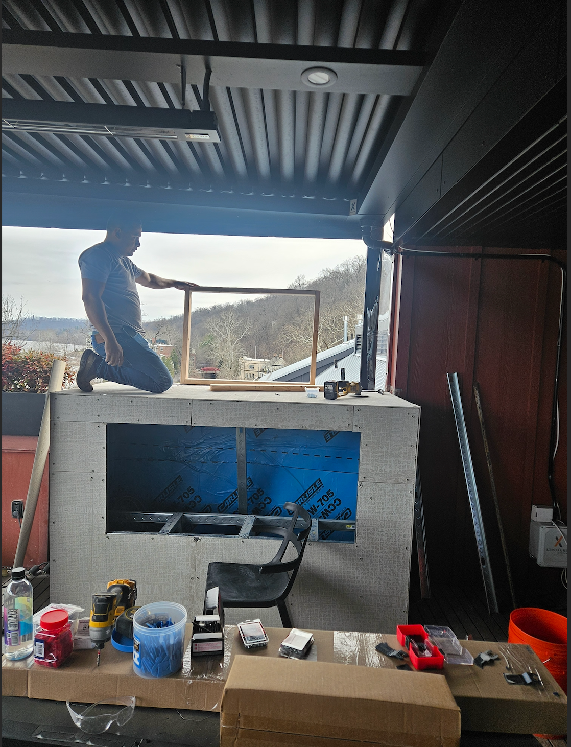 Covered outdoor kitchen with a grill, workbench, hanging fish, and a dark corrugated roof overhead