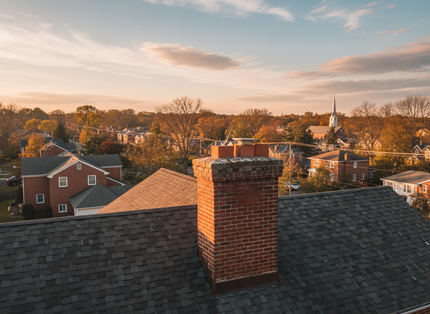 Rooftops and brick chimney overlooking a small town at sunset with warm autumn trees.