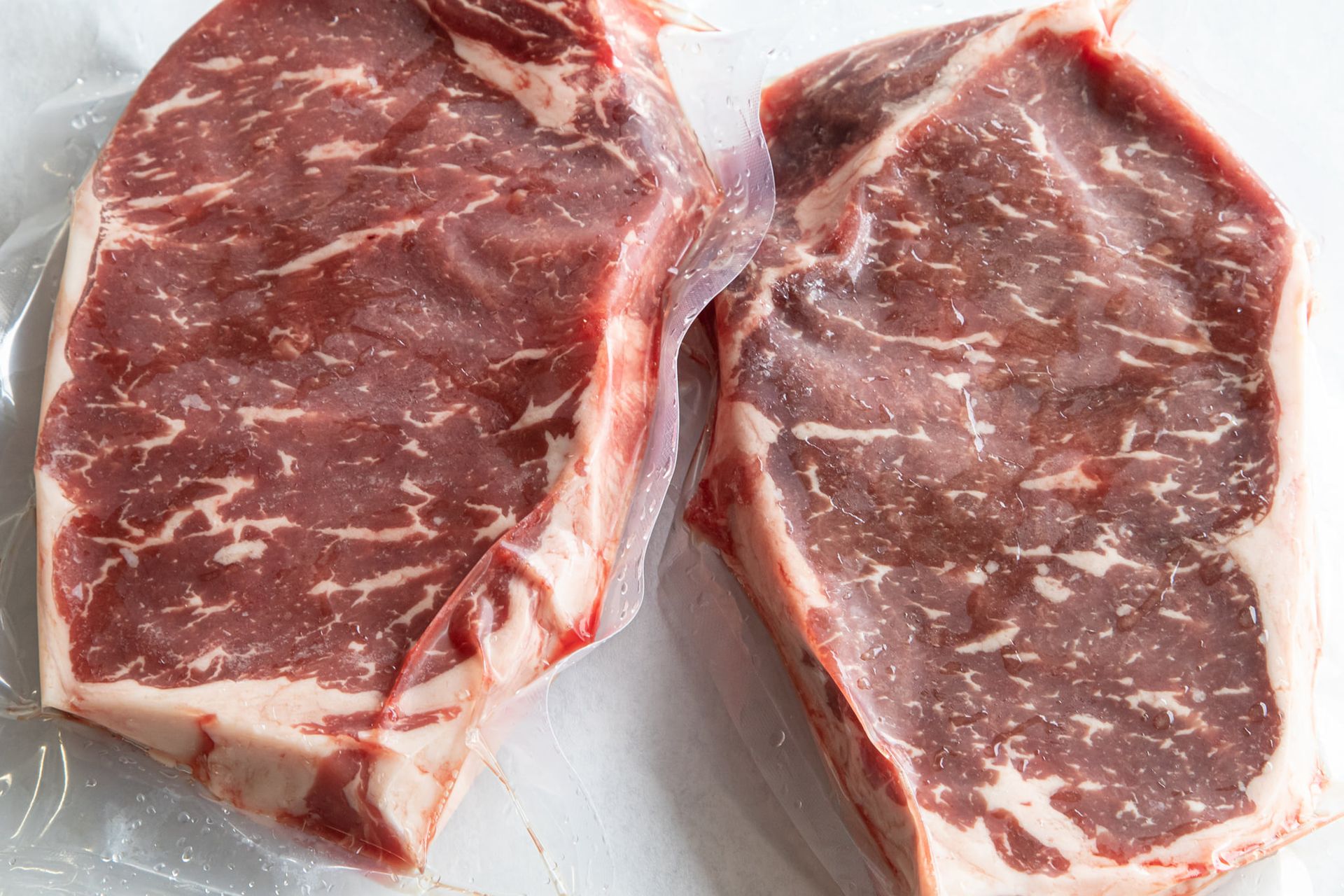 Two steaks are wrapped in plastic and sitting on a table.