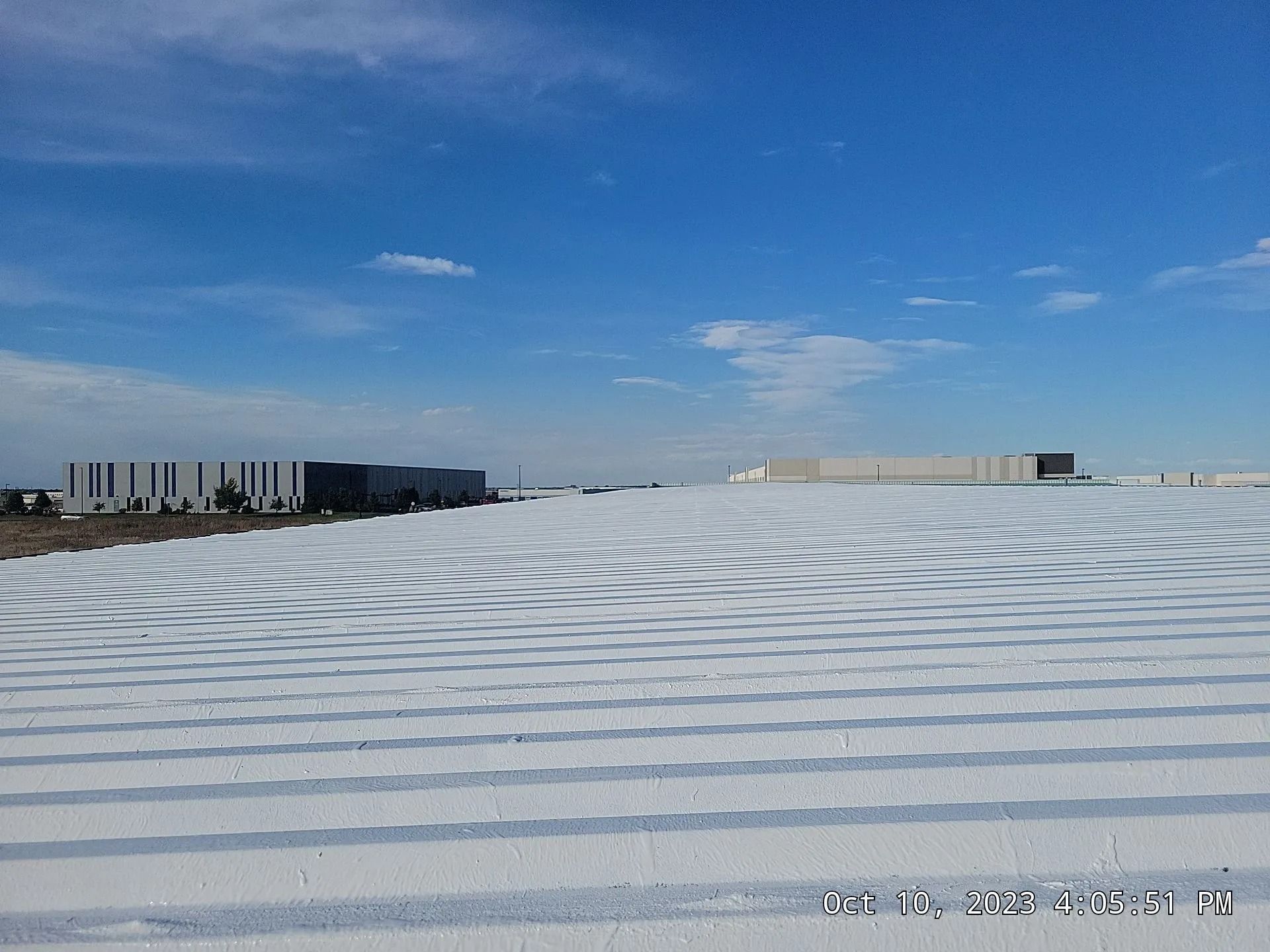 White industrial roof, blue sky. Buildings in the background.