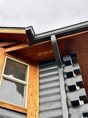 Black gutter and downspout on a wooden house with a window.