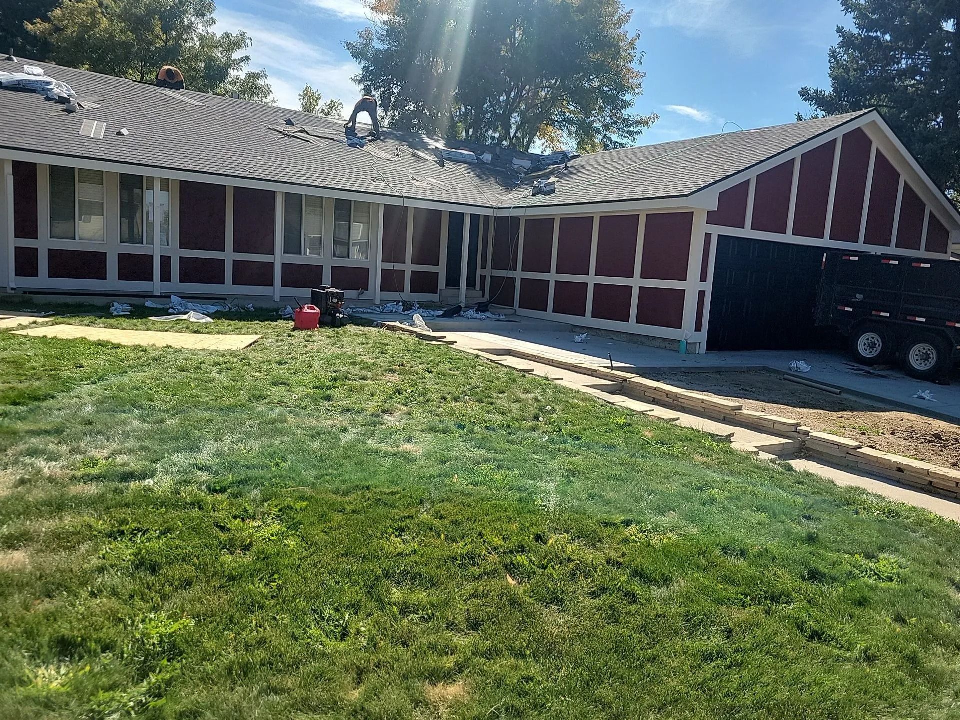House with red siding and a dark roof. Roofing work in progress, lawn in front.