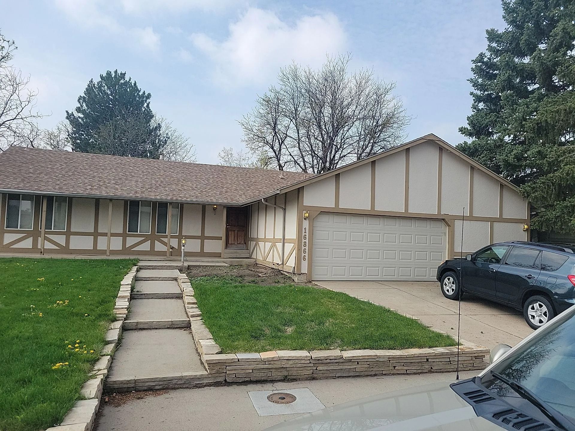Ranch-style house with beige trim and a two-car garage. Black car parked in the driveway, green lawn.
