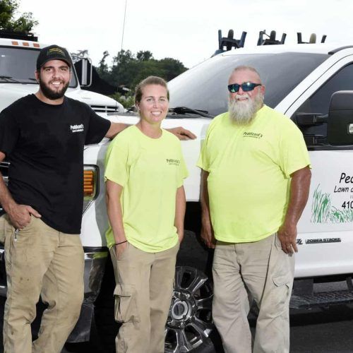 Three people standing in front of a white service truck, wearing work uniforms, smiling.