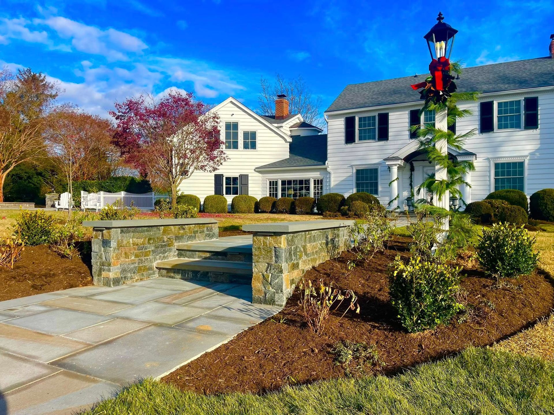 A white two-story house with a stone pathway and a decorative lamp post in the front yard on a bright, sunny day.