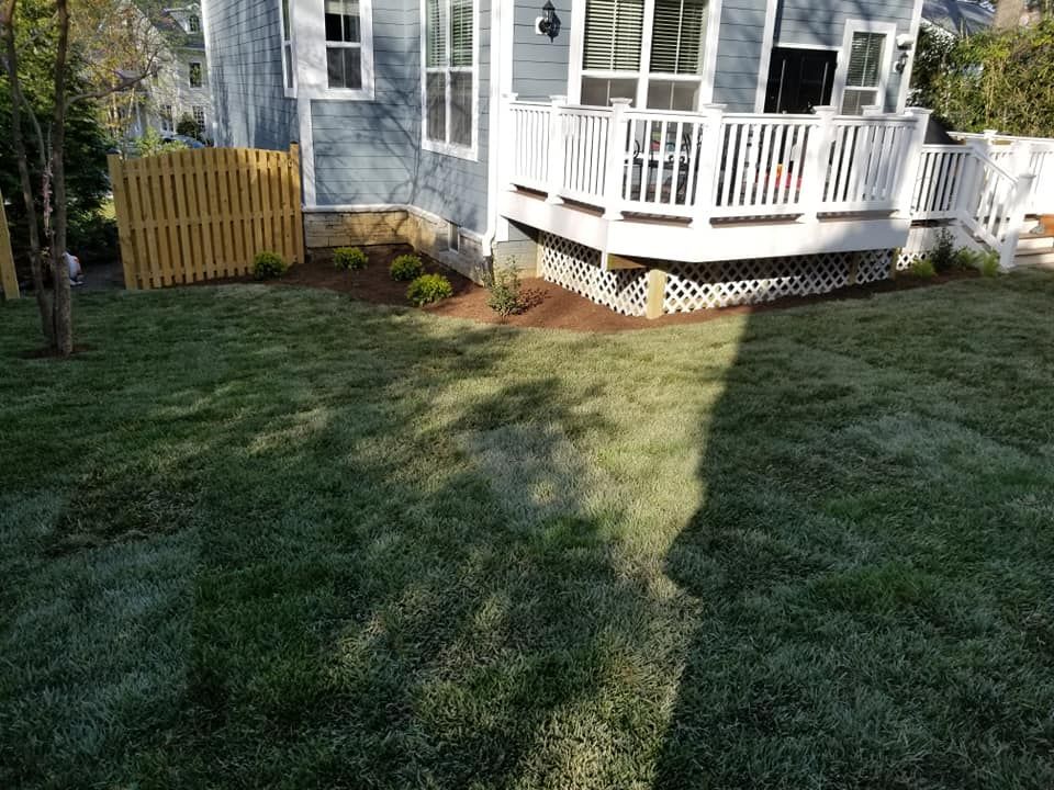 A blue house with a white deck and lattice skirting, featuring a freshly laid lawn and a small yellow picket fence.