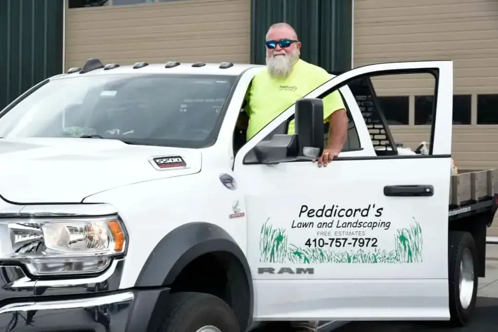 A person in a bright yellow shirt stands beside a white Ram work truck labeled 