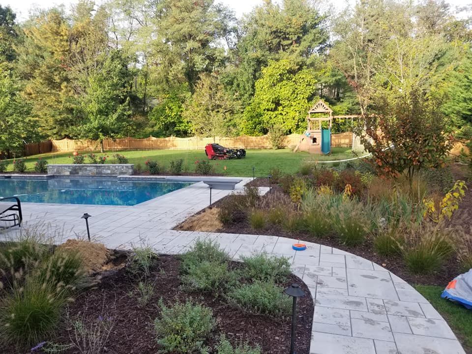 A swimming pool with stone pavers and a landscaped yard featuring a small wooden playground set and green trees.