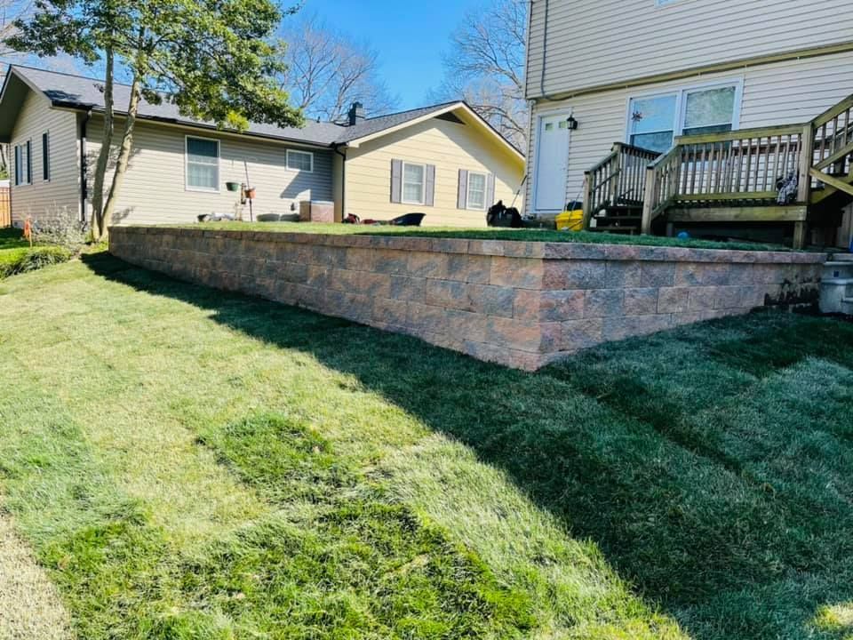 A newly installed multi-colored stone retaining wall in a backyard with freshly laid sod grass on a sunny day.