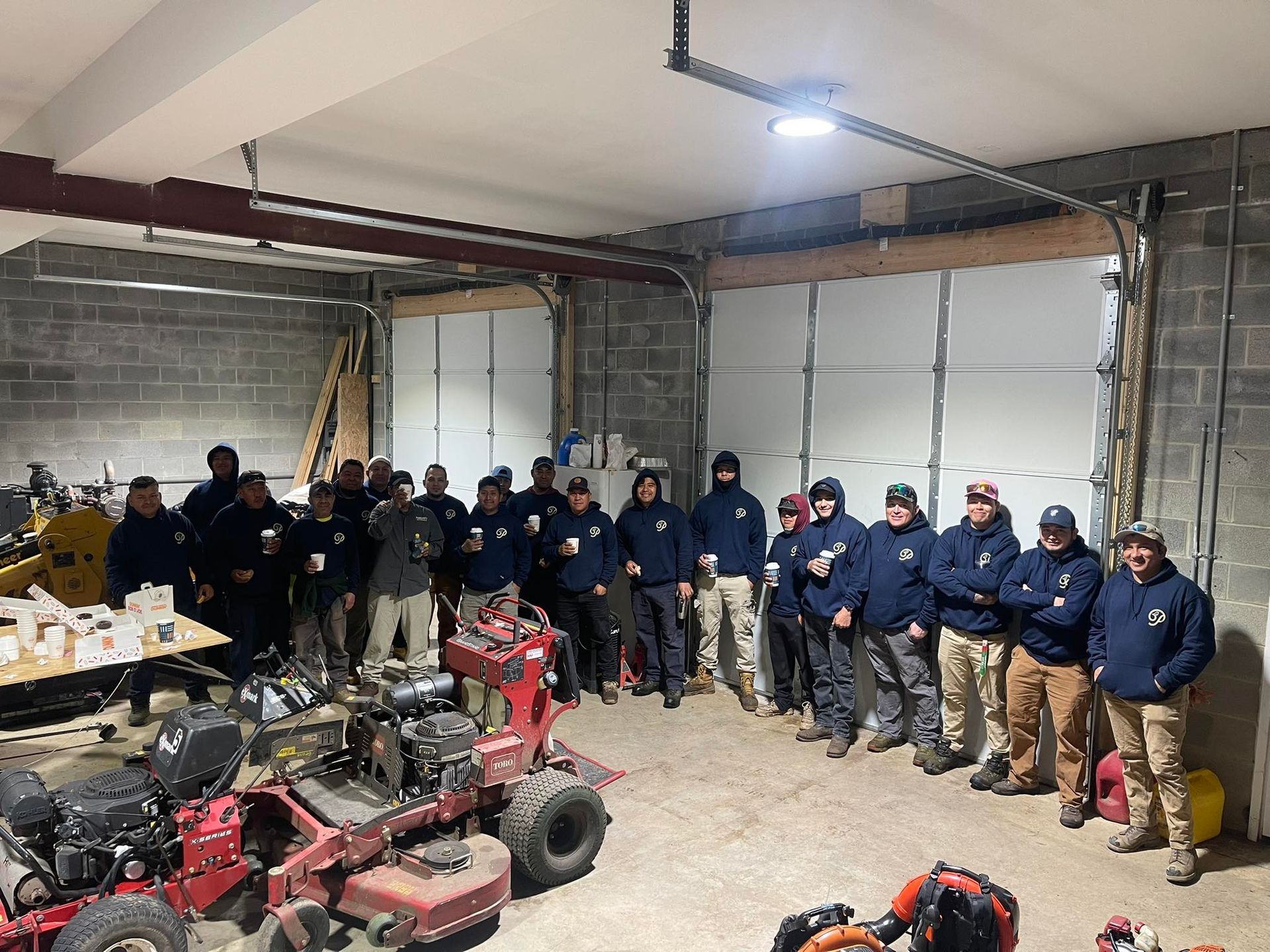 A group of people in blue uniforms standing in a garage beside ATVs and tools