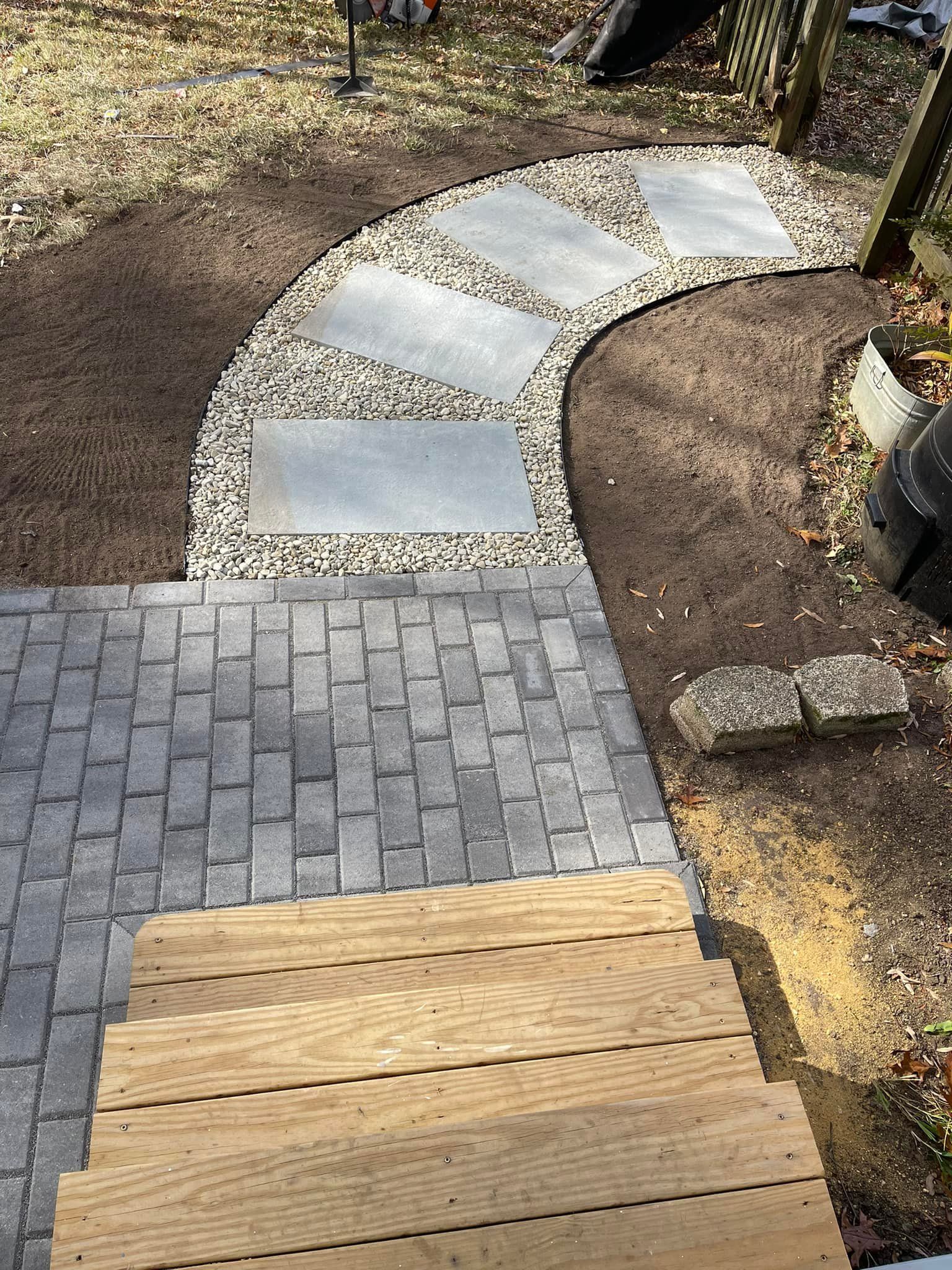 A wooden staircase leading to a gray paver patio and a curved path of stone stepping stones set in gravel.