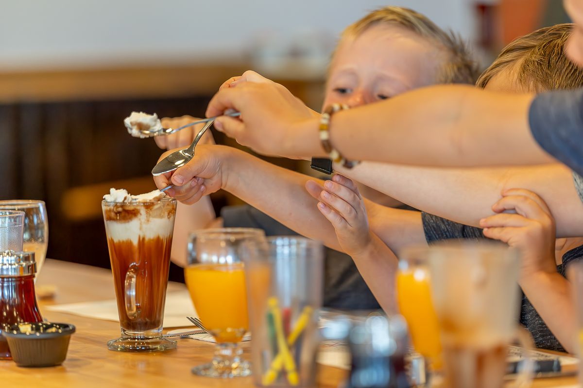 Children reaching for whipped cream on a sundae in a restaurant, focus on hands and dessert.