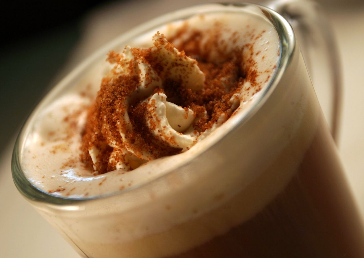 Close-up of a clear glass mug filled with layered coffee drink, whipped cream, and cinnamon.
