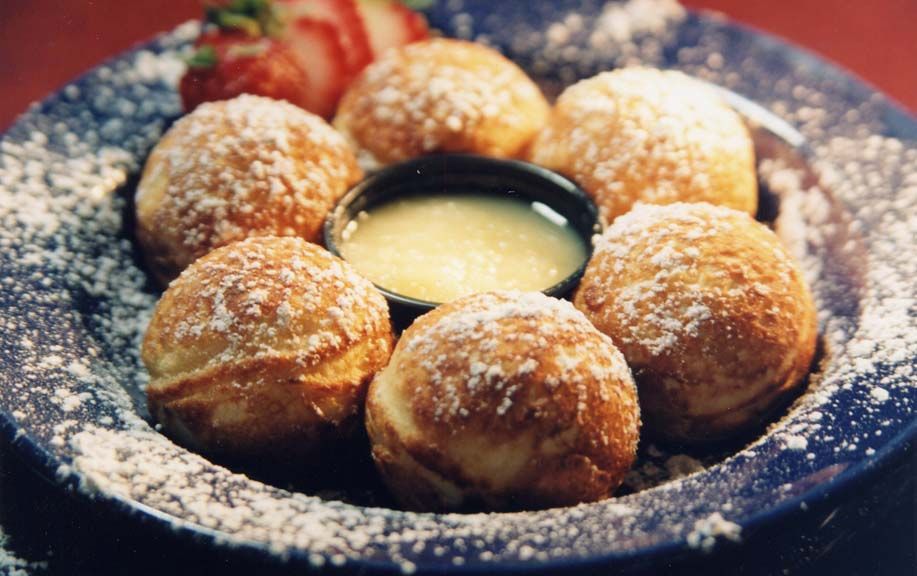 Seven round, golden-brown pancakes dusted with powdered sugar, served on a blue plate with creamy sauce in the center, and a strawberry.