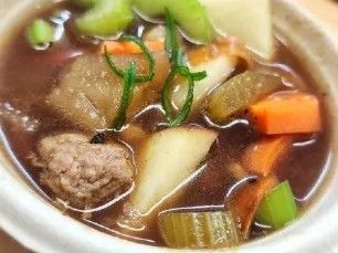 A bowl of soup with meatballs , carrots , celery and potatoes.