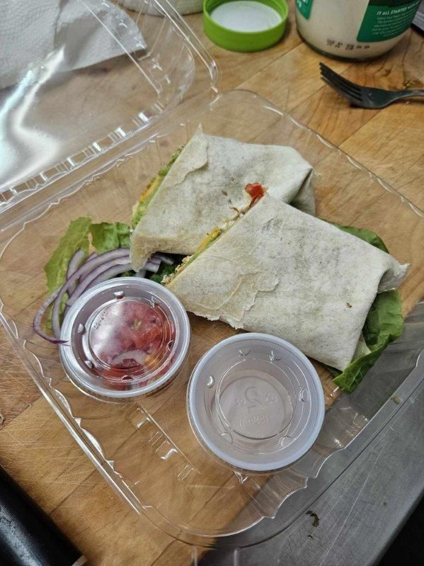 A tortilla wrap is in a plastic container on a wooden table.