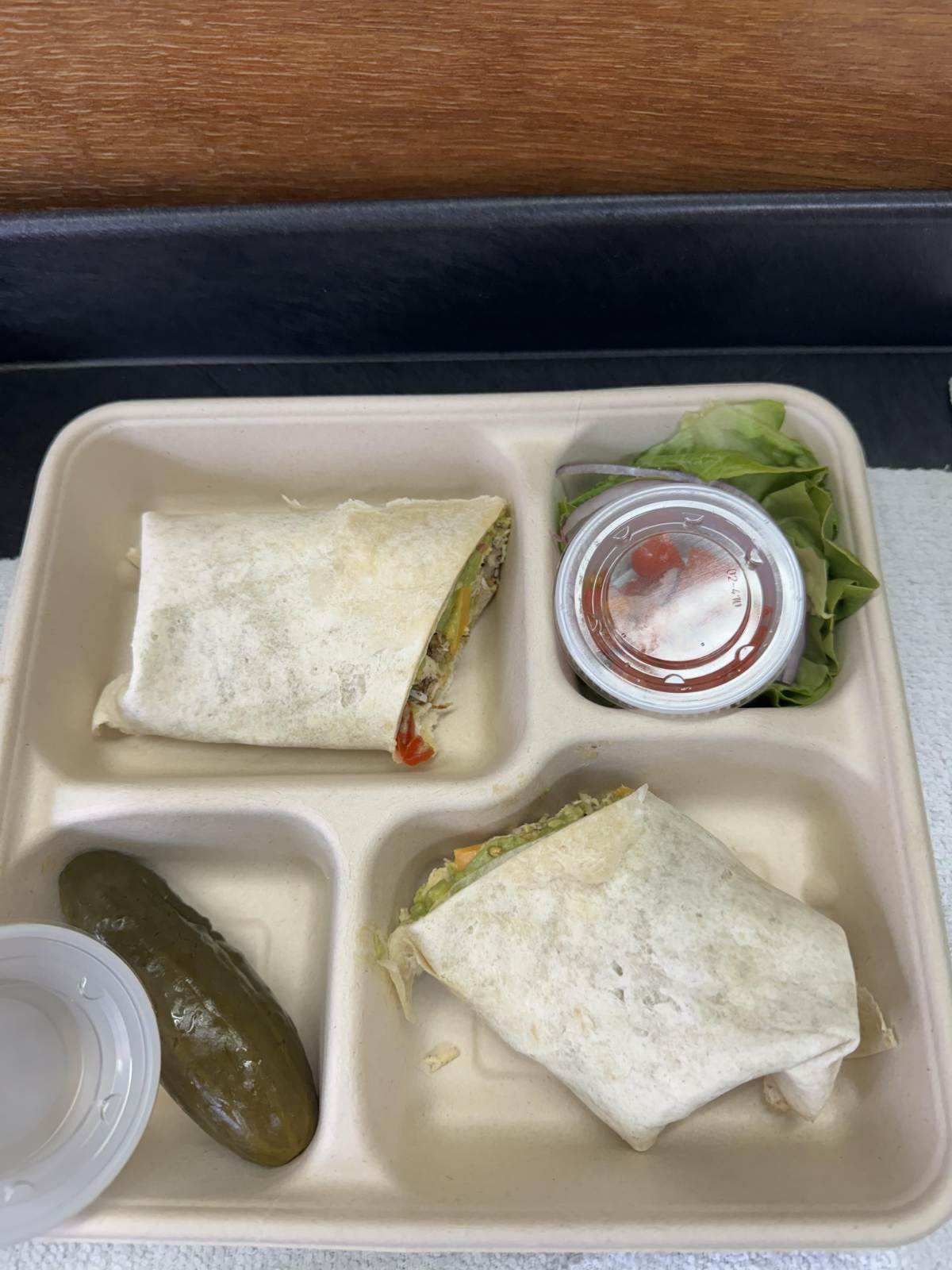 A plastic tray filled with a sandwich, pickles, and sauce.