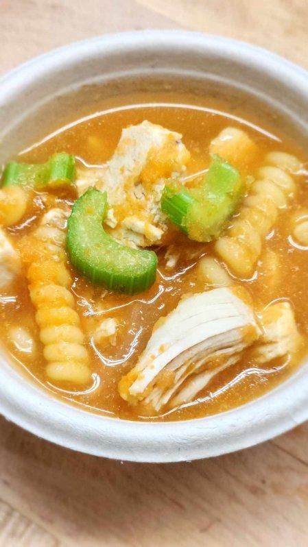 A bowl of soup with noodles and celery on a wooden table.