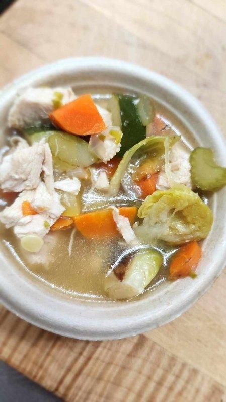 A bowl of soup with chicken and vegetables on a wooden table.