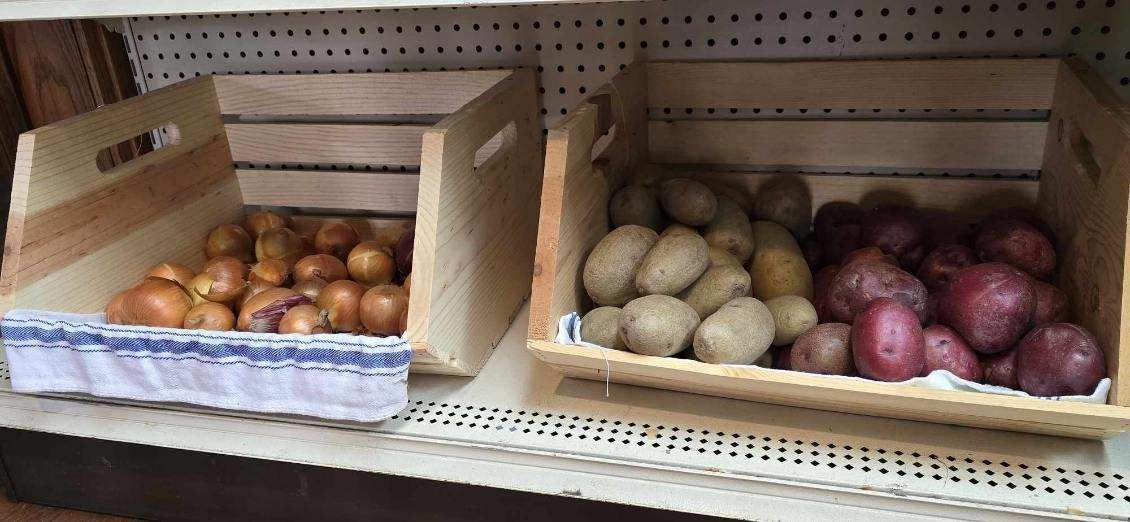Two wooden crates filled with potatoes and onions are on a shelf.