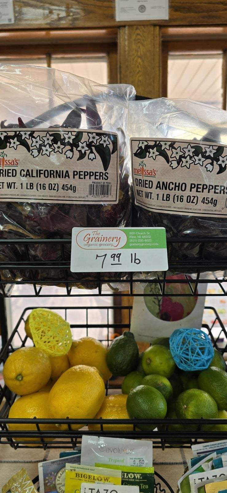 A basket of lemons and limes on a shelf in a store.