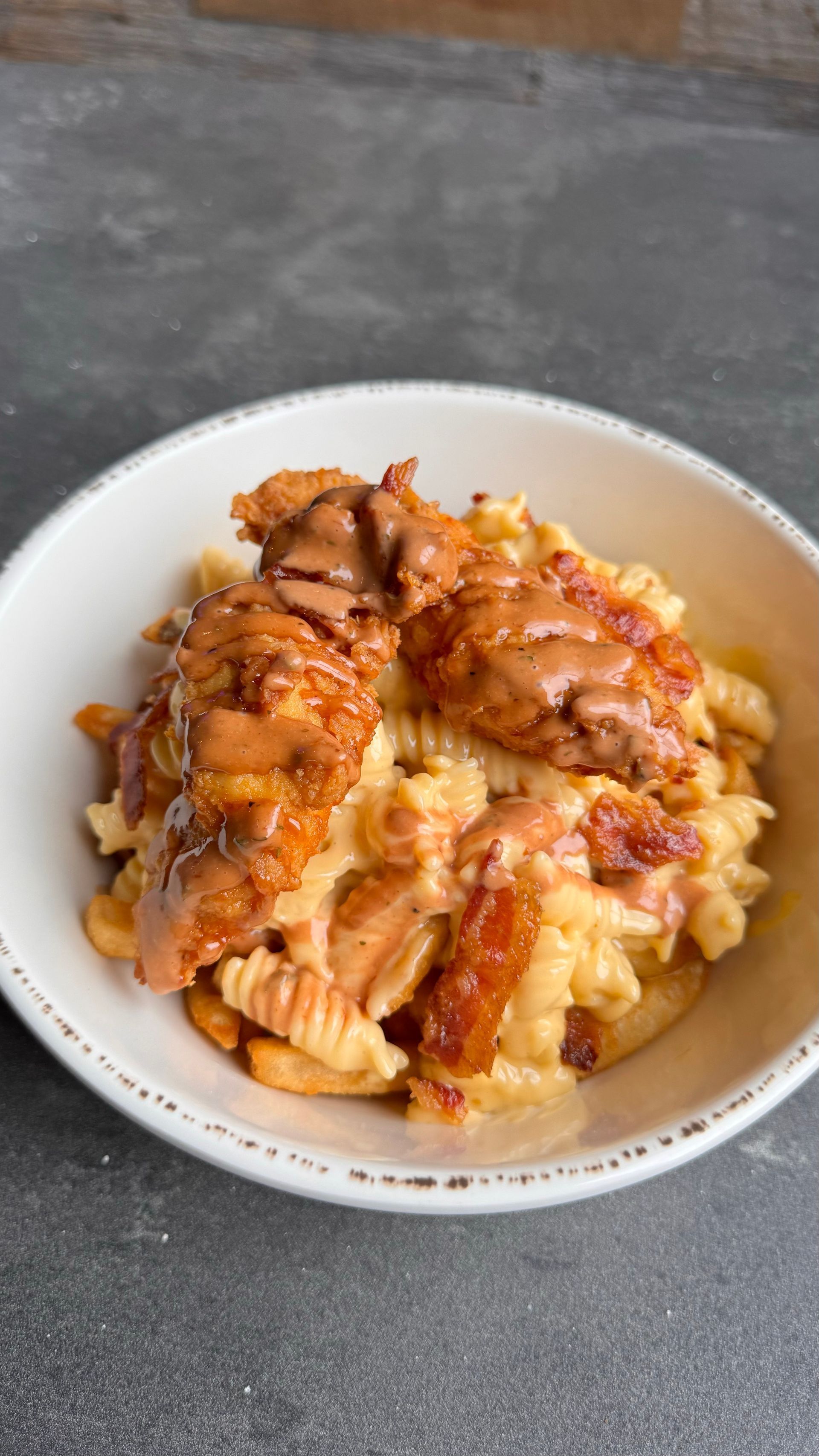 Mac and cheese with fried chicken and brown sauce, served in a white bowl.