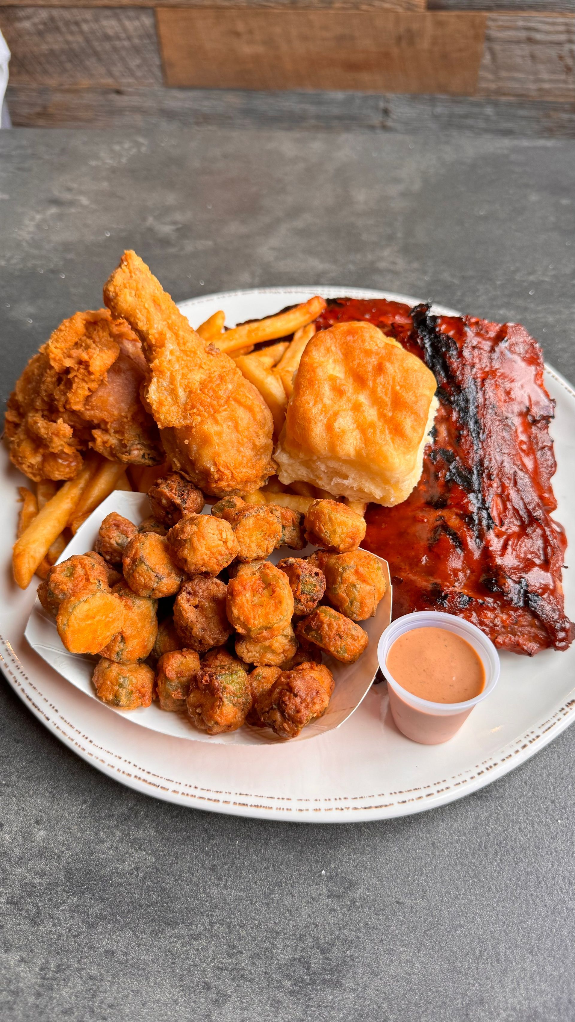 Plate of fried chicken, ribs, fries, okra, and a biscuit with dipping sauce.