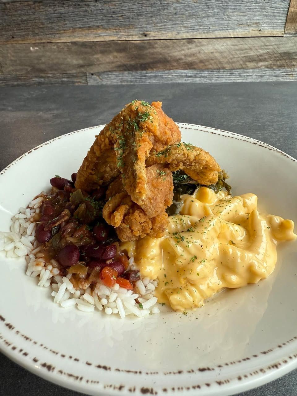 Plate of Southern comfort food: fried chicken wings, mac and cheese, collard greens, and red beans with rice.