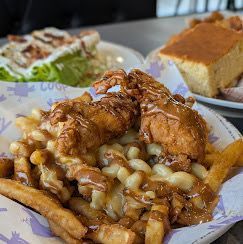 Fried chicken poutine with gravy on fries, salad, and cornbread in the background.