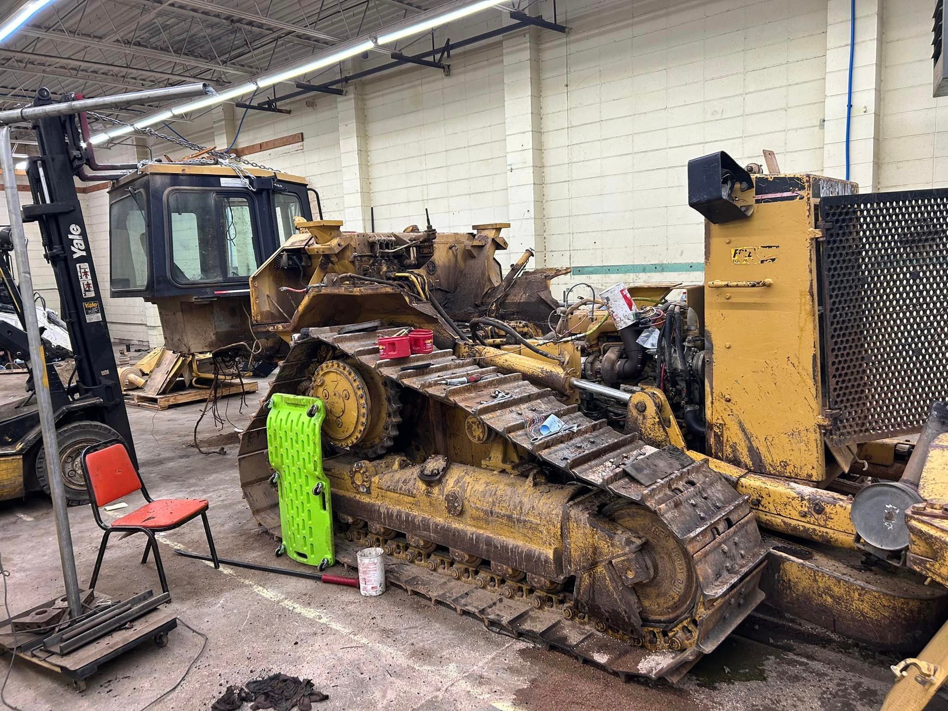 A bulldozer is sitting in a garage next to a forklift.