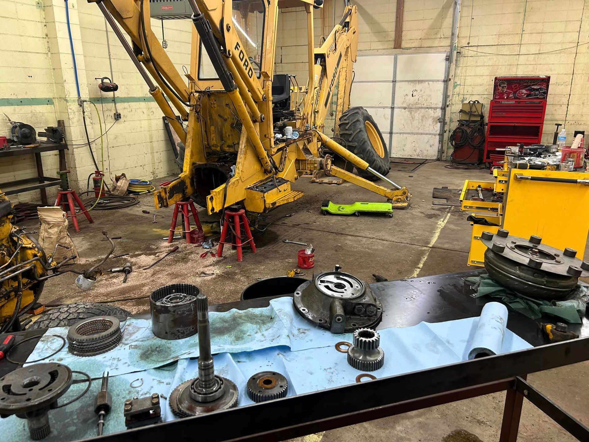 A yellow tractor is being repaired in a garage.