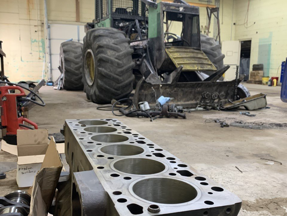 A tractor is being repaired in a garage with a cylinder block in the foreground.