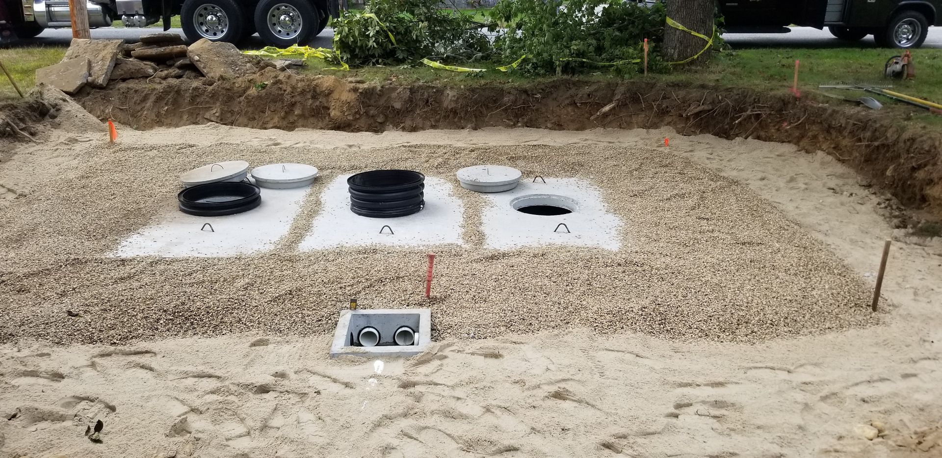 A septic system being installed in a gravel-filled trench. Concrete lids and pipes are visible.