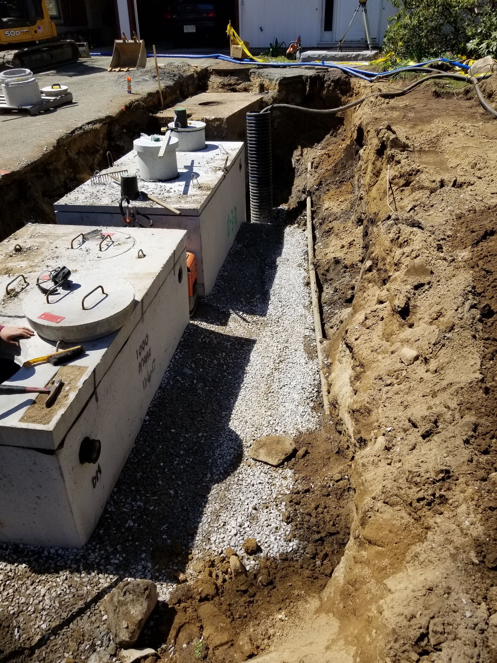Trench dug in the ground with two large concrete tanks in it; gravel bed below the tanks.