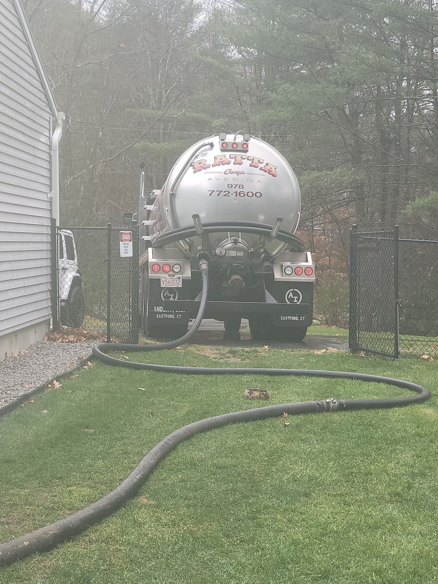 A septic tank truck is parked in front of a house with a hose attached to it.
