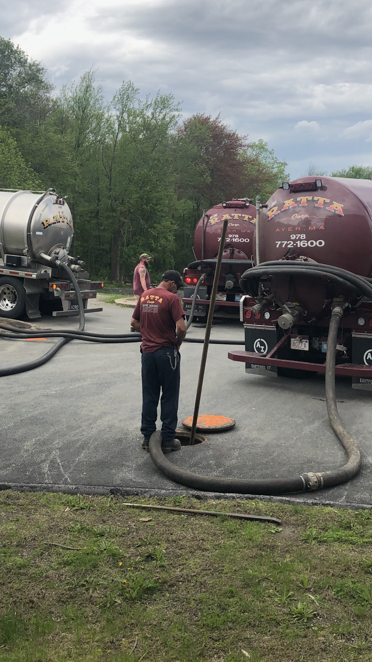 A man is standing next to a vacuum truck in a parking lot.