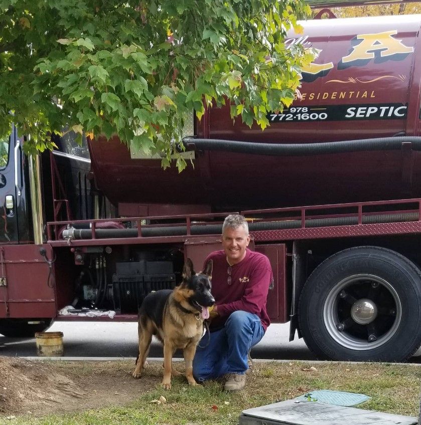 A man kneeling next to a german shepherd in front of a septic truck
