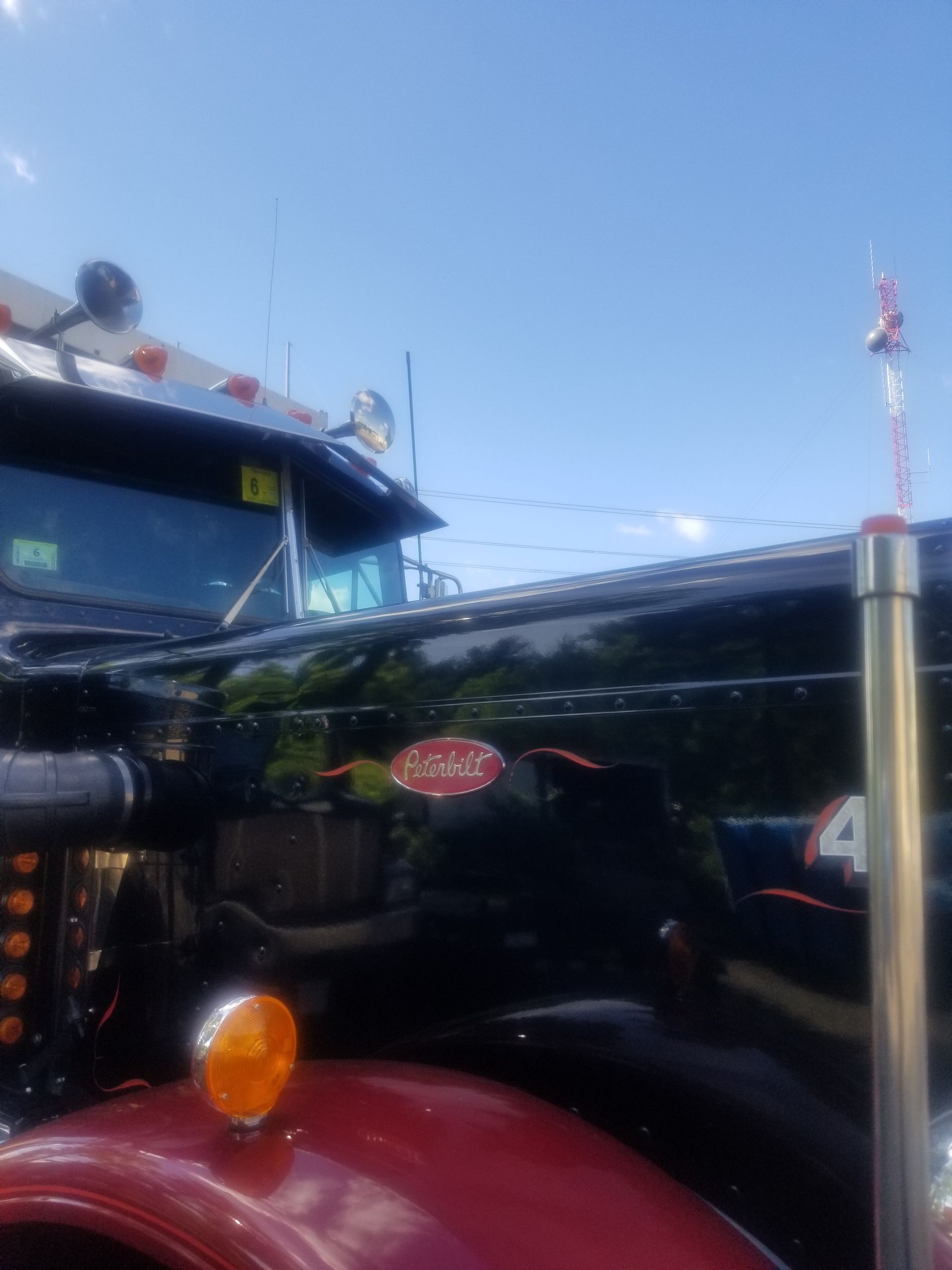 Black Peterbilt semi-truck with red accents and the Peterbilt logo against a blue sky.