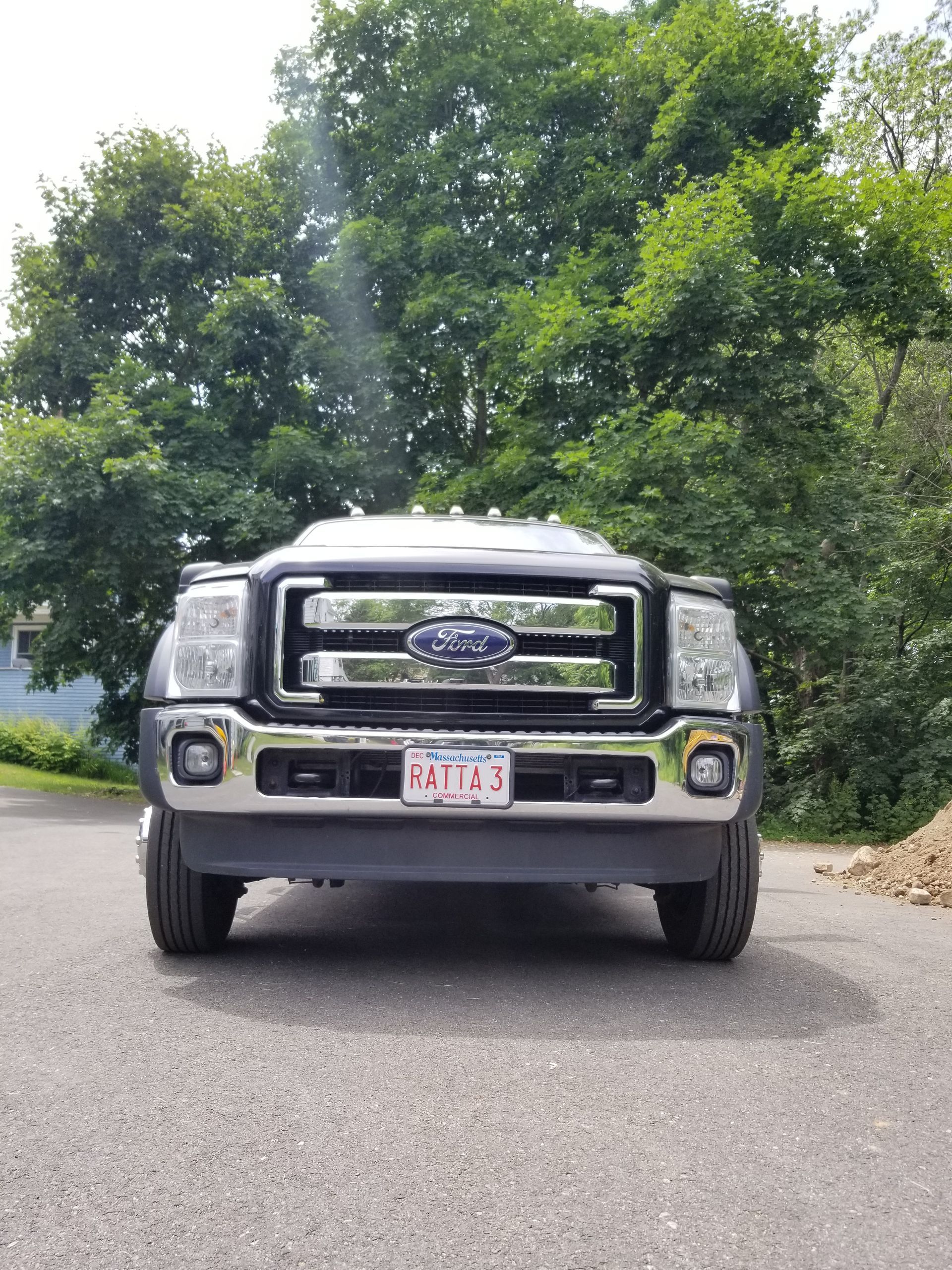A dark gray Ford truck parked on a driveway, Massachusetts license plate visible, with a green tree background.