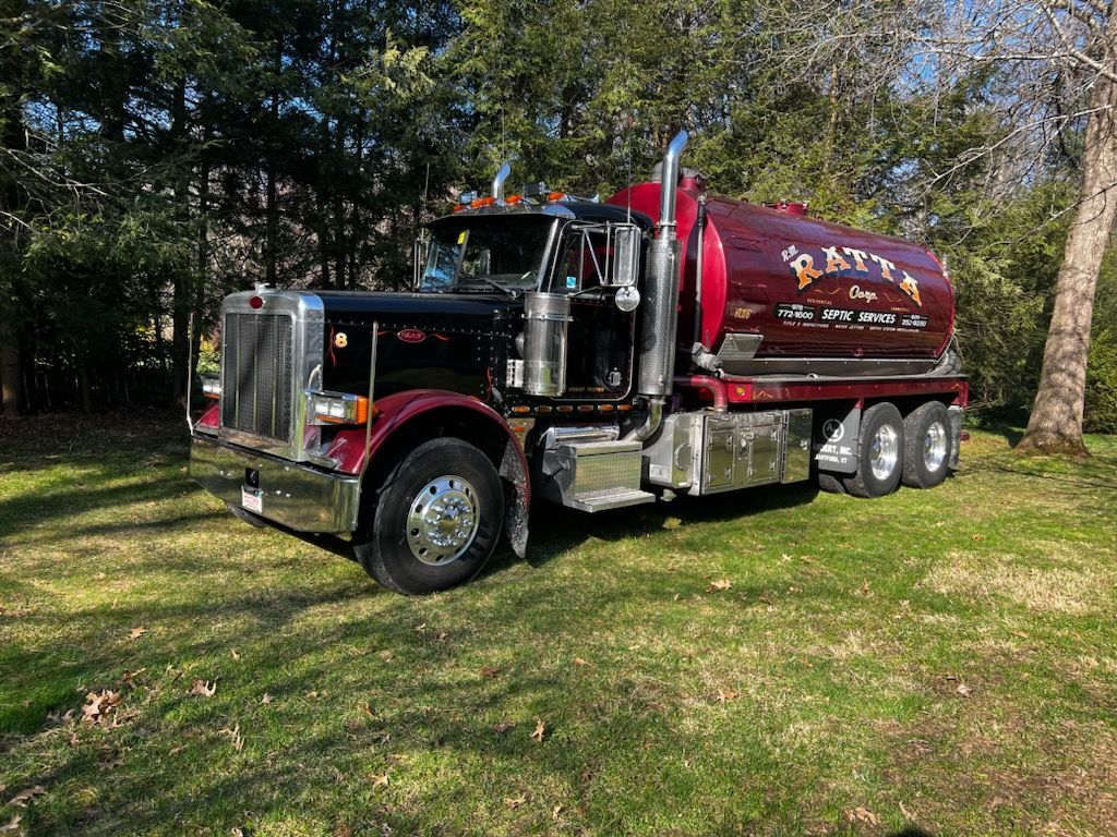 A burgundy and black tanker truck parked on a grassy lawn in front of trees. The truck has chrome accents.