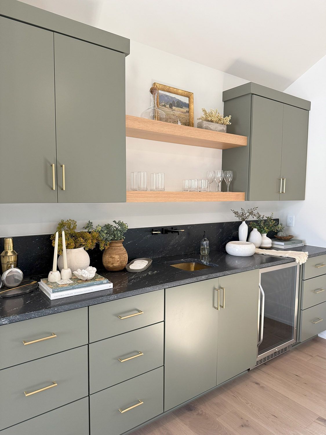 A kitchen with gray cabinets, black counter tops, and a stainless steel dishwasher.
