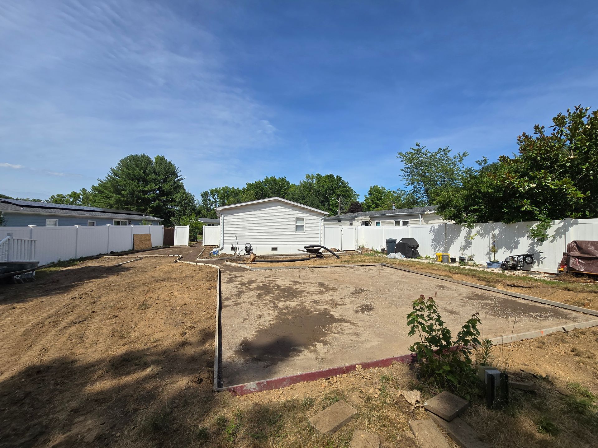 A dirt yard with a white fence and a house in the background