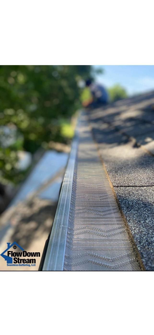 A close-up view of a metal mesh gutter guard installed on a residential roof, with a blurred worker in the background.
