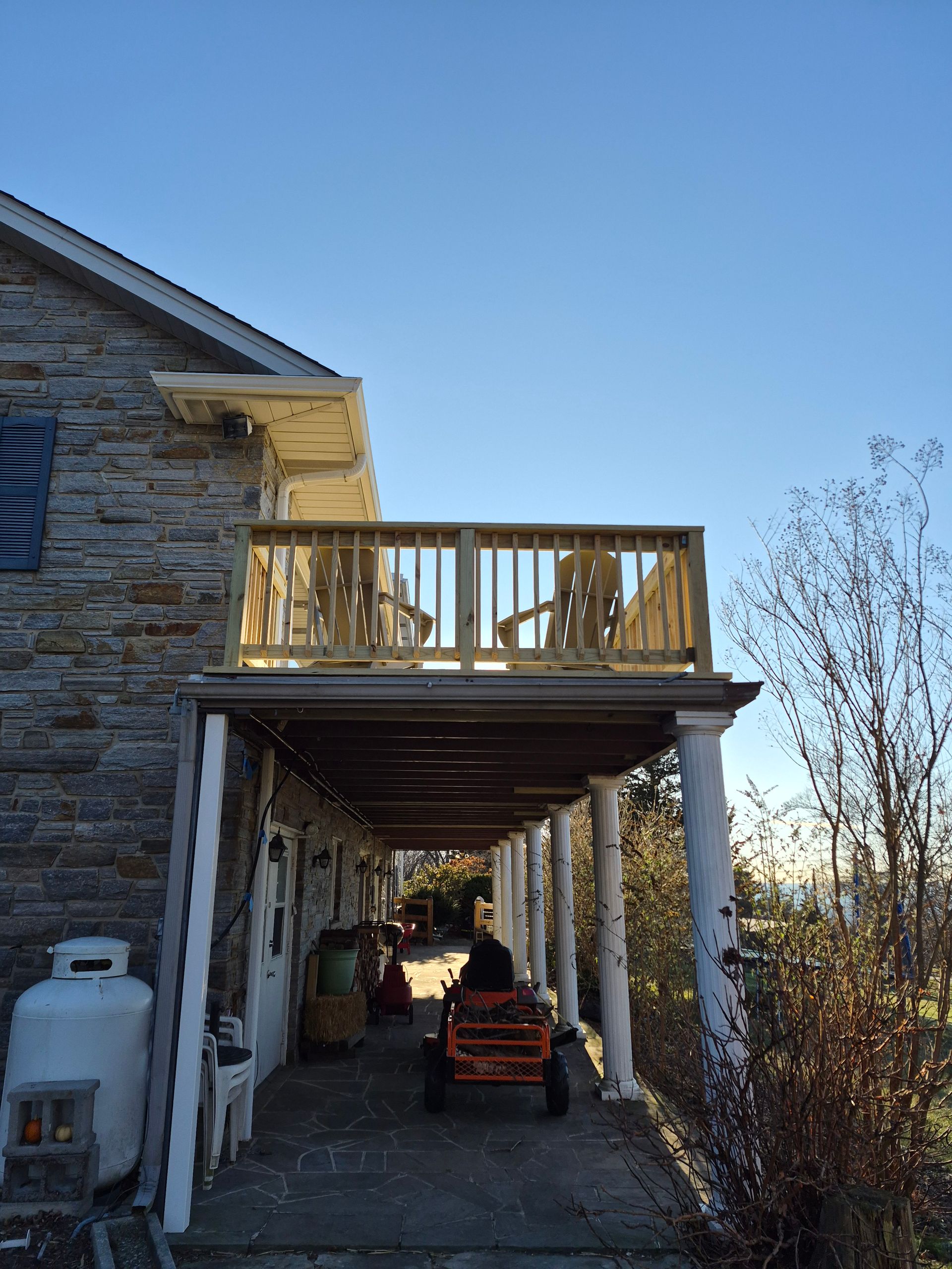 Two-story house with a wooden deck above a covered porch; two chairs sit on the deck, sunny day.
