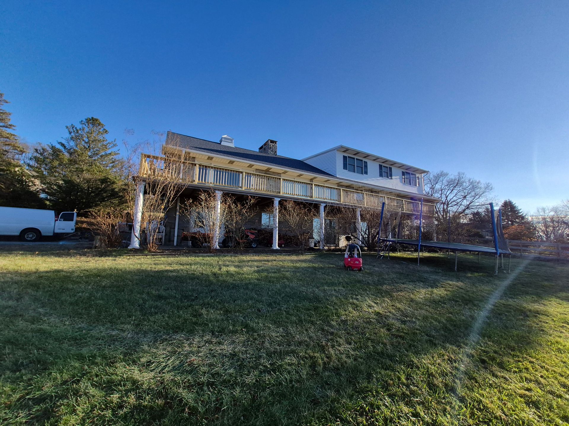 House with wrap-around porch and white pillars on a grassy lawn under a clear, blue sky.