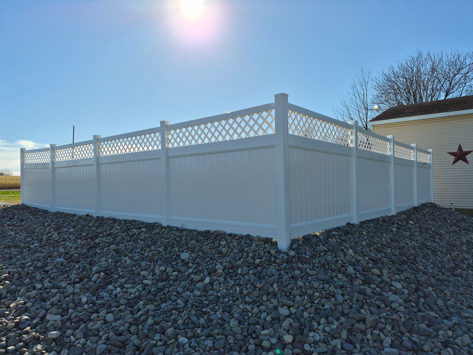 White vinyl fence with lattice top surrounds gravel yard on a sunny day.