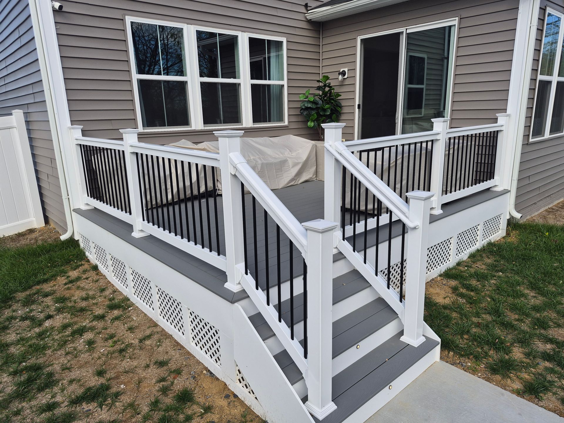 Gray and white deck with black railings and steps leading to a house with gray siding.