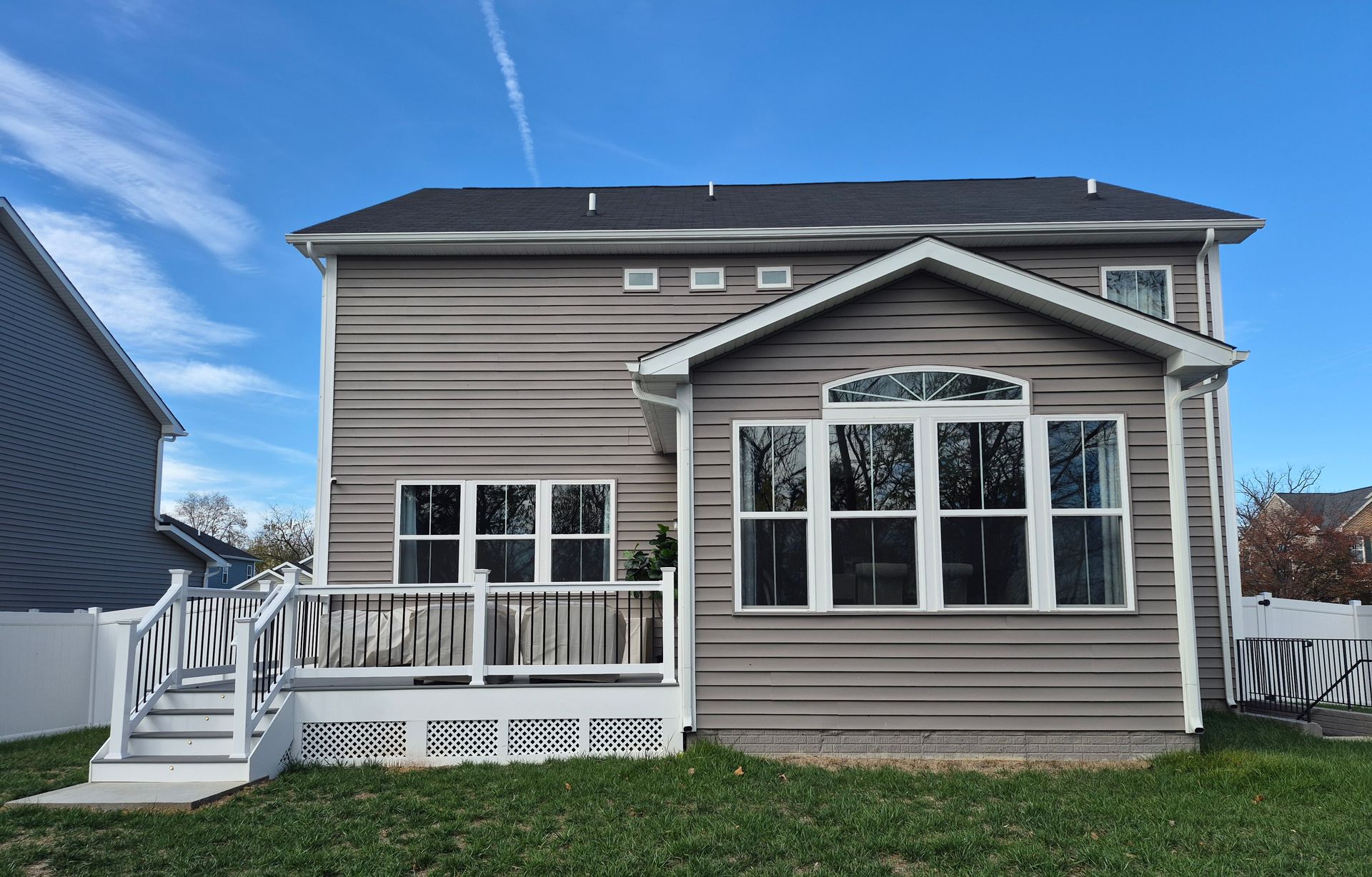 Back view of a two-story house with a sunroom, deck, and gray siding against a blue sky.